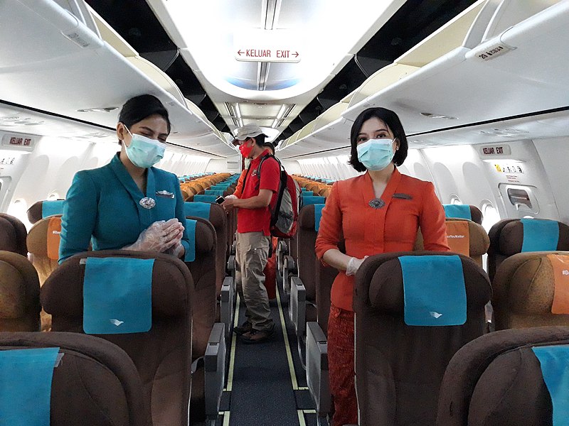 Cabin crew members wearing PPE greet passengers